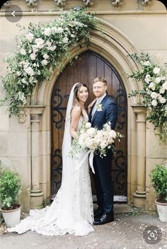 a bride and groom standing in front of an arched doorway with greenery on either side