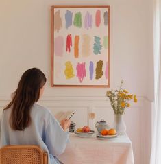 a woman sitting at a table in front of a plate of fruit and an open book