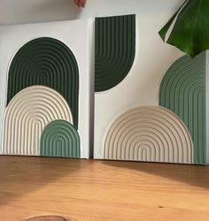 two green and white art pieces sitting on top of a wooden table next to a plant