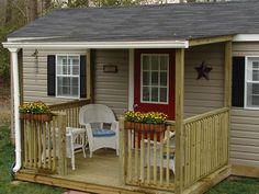 a small wooden porch with two chairs and a table on the front deck next to a red door