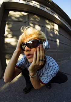 a woman wearing sunglasses and headphones sitting in front of a garage door while listening to music