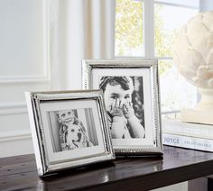 two silver frames sitting on top of a wooden table next to a vase with flowers