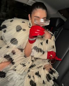 a woman in a dress and red gloves is sitting in the back seat of a car