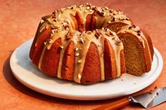 a bundt cake with frosting and nuts on top sitting on a plate next to a knife