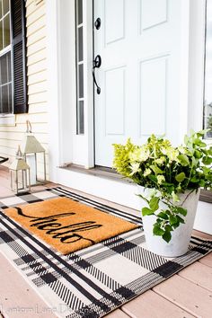 a potted plant is sitting on the front porch with a welcome mat and lantern