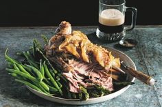 a plate with meat, asparagus and green beans next to a glass of beer