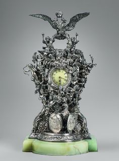 an ornate clock is sitting on top of a green marble base with silver and white decorations