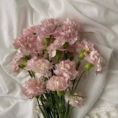 pink carnations are arranged in a vase on a white cloth covered bed sheet