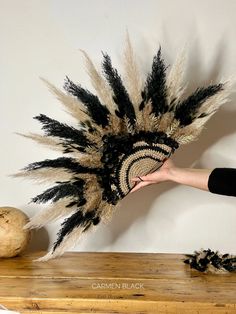 a woman is holding a hat with feathers on it, and another item in the background