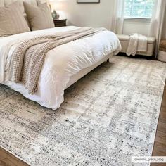 a large white bed sitting on top of a wooden floor next to a window in a bedroom