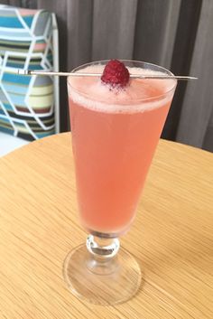 a drink with a raspberry garnish on the rim sits on a table