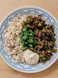 a white and blue plate topped with rice, meat and veggies next to sour cream