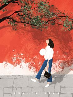 a woman walking down the street in front of a red wall with a tree on it