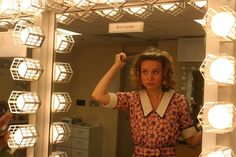 a woman standing in front of a mirror holding her arm up to her head and looking into the mirror