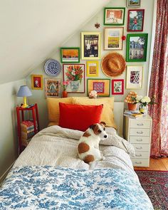 a dog laying on top of a bed in a bedroom next to a wall full of pictures