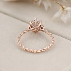 a close up view of a rose gold engagement ring on a white cloth with flowers in the background