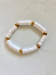 a white and gold beaded bracelet on a marble counter top with two gold beads