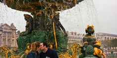 a man and woman kissing in front of a fountain