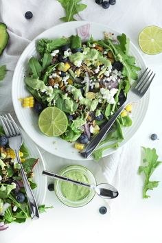 two plates filled with salad next to an avocado on a white tablecloth