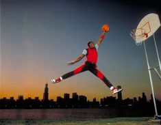 a man jumping up into the air to dunk a basketball in front of a city skyline