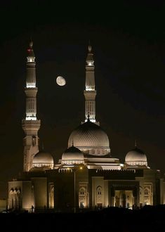 two large white buildings with lights on them and the moon in the sky behind them