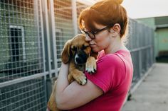 a woman is holding a puppy in her arms and looking at the fence behind her