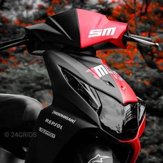 a red and black scooter parked in front of some trees