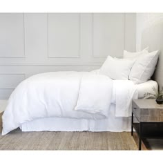 a bed with white linens and pillows in a small room next to a wall