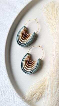 two pairs of earrings sitting on top of a white plate next to some dry grass