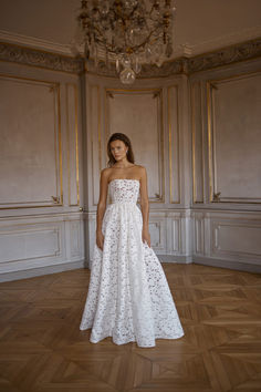 a woman in a white dress standing on a wooden floor next to a chandelier