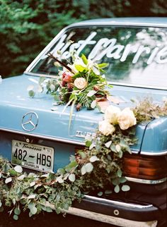 an old blue car with flowers and greenery on it