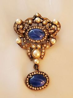 "Quality abounds in this spectacular brooch and pendant, signed DeNicola. It's in the most excellent condition and embodies the outstanding design elements of the finest costume jewelry. DeNicola is revered for for some of its finest lines of jewelry, and this brooch in no exception to that quality. The flawed sapphires are sensational and combine with pearls and tiny rhinestones to enchant its design. Every stone is perfect. A pendant detachment is built into the construction of the back and al Antique Jeweled Pendant Brooches, Vintage Pendant Brooches With Cabochon, Vintage Jeweled Brooch For Anniversary, Oval Brooch For Vintage Events, Vintage Jeweled Brooches For Anniversary, Vintage Jewel Brooches For Anniversary, Vintage Jewels Brooches For Anniversary, Vintage Jeweled Anniversary Brooch, Vintage Hallmarked Pendant Brooches