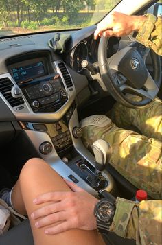 a soldier is sitting in the driver's seat of a car with his hand on the steering wheel