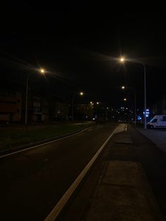 an empty street at night with lights on and cars parked along the side of the road