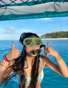 a woman wearing goggles and giving the thumbs up sign while standing on a boat