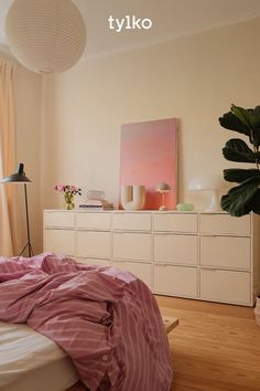 a bedroom with a bed, dresser and plant