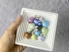 a hand holding a small white bowl filled with assorted colored glass beads in it