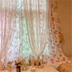 there is a table with flowers on it in front of the window and curtains behind it