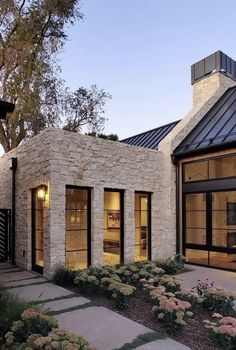 a stone house with large windows and flowers in the front yard