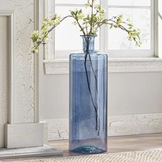 a blue vase with flowers in it sitting on the floor next to a window sill