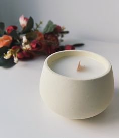 a white candle sitting on top of a table next to flowers