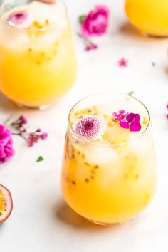 two glasses filled with drinks sitting on top of a white table next to pink flowers