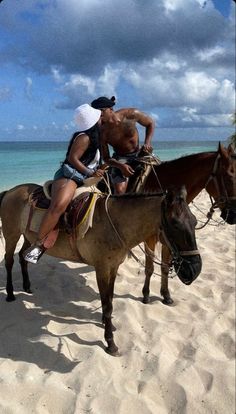 two men riding horses on the beach with blue water in the backgrouds