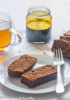 two pieces of brownie on a plate with a fork and cup of tea next to it