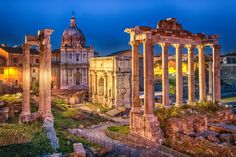 the ruins of an old roman city at night with lights on and buildings in the background