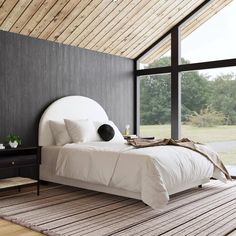 a large bed sitting in a bedroom next to a tall window on top of a wooden floor