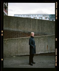 a man standing in an empty parking lot next to a brick wall and some buildings