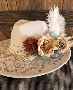 a white hat with flowers and feathers on top of a furnishing area next to a wooden wall