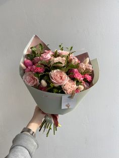 a person holding a bouquet of pink flowers in their hand with a white wall behind them