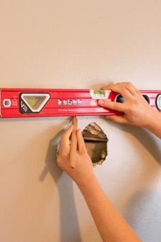 a woman is measuring the wall with a large red ruler on it's side